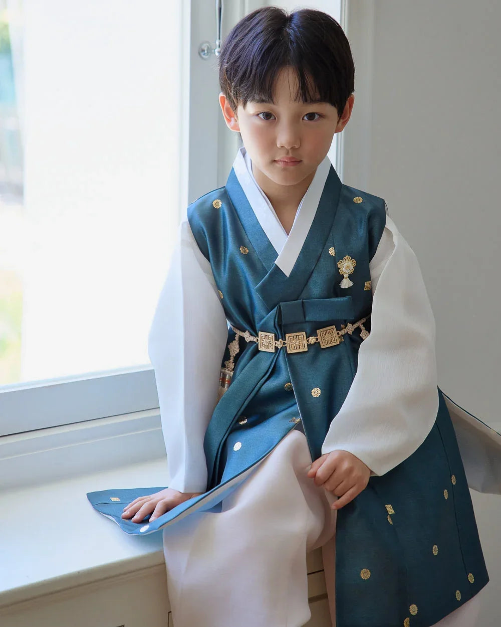 A boy wearing a teal Native Korean Boy Hanbok with gold embroidery and a decorative belt.