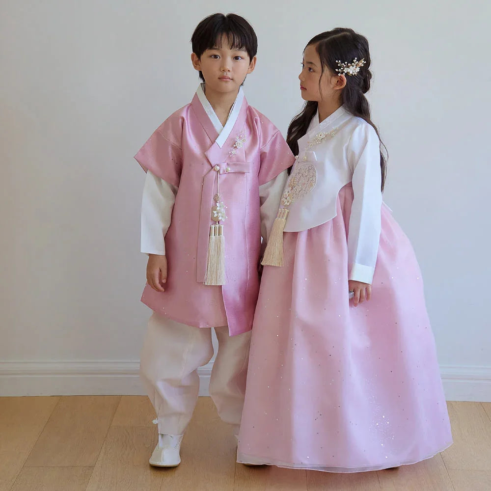 A boy and girl wearing pearl pink Native Korean hanbok with traditional norigae accessories.
