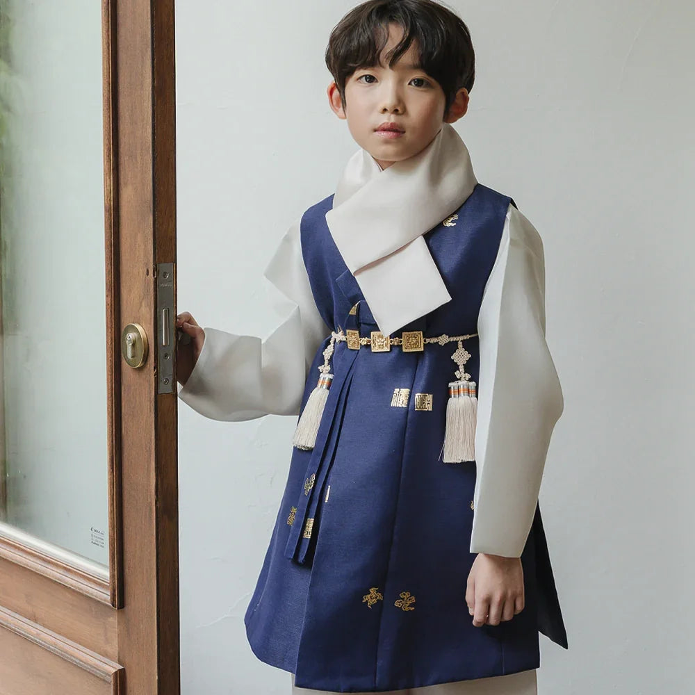 A boy wearing a navy blue Native Korean boy hanbok with a white scarf and decorative norigae.
