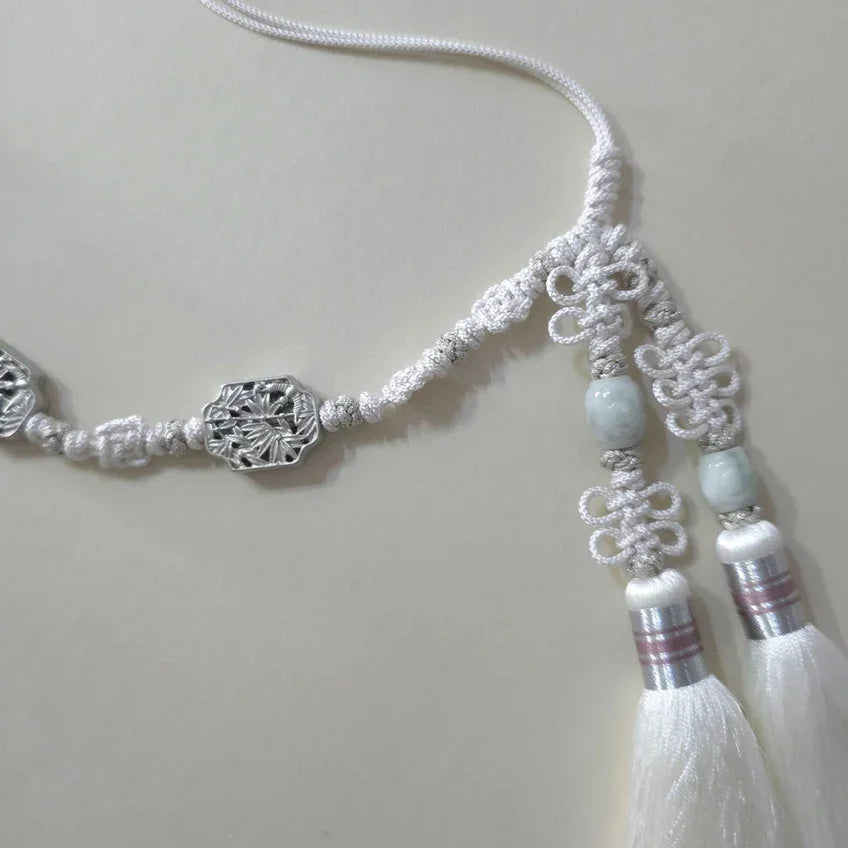 Close-up of a white Native Korean Norigae tassel with silver ornaments and jade beads.