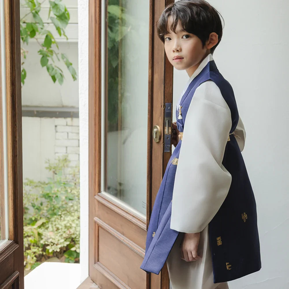 A boy wearing a Native Korean navy blue and white boy hanbok standing by a wooden door.