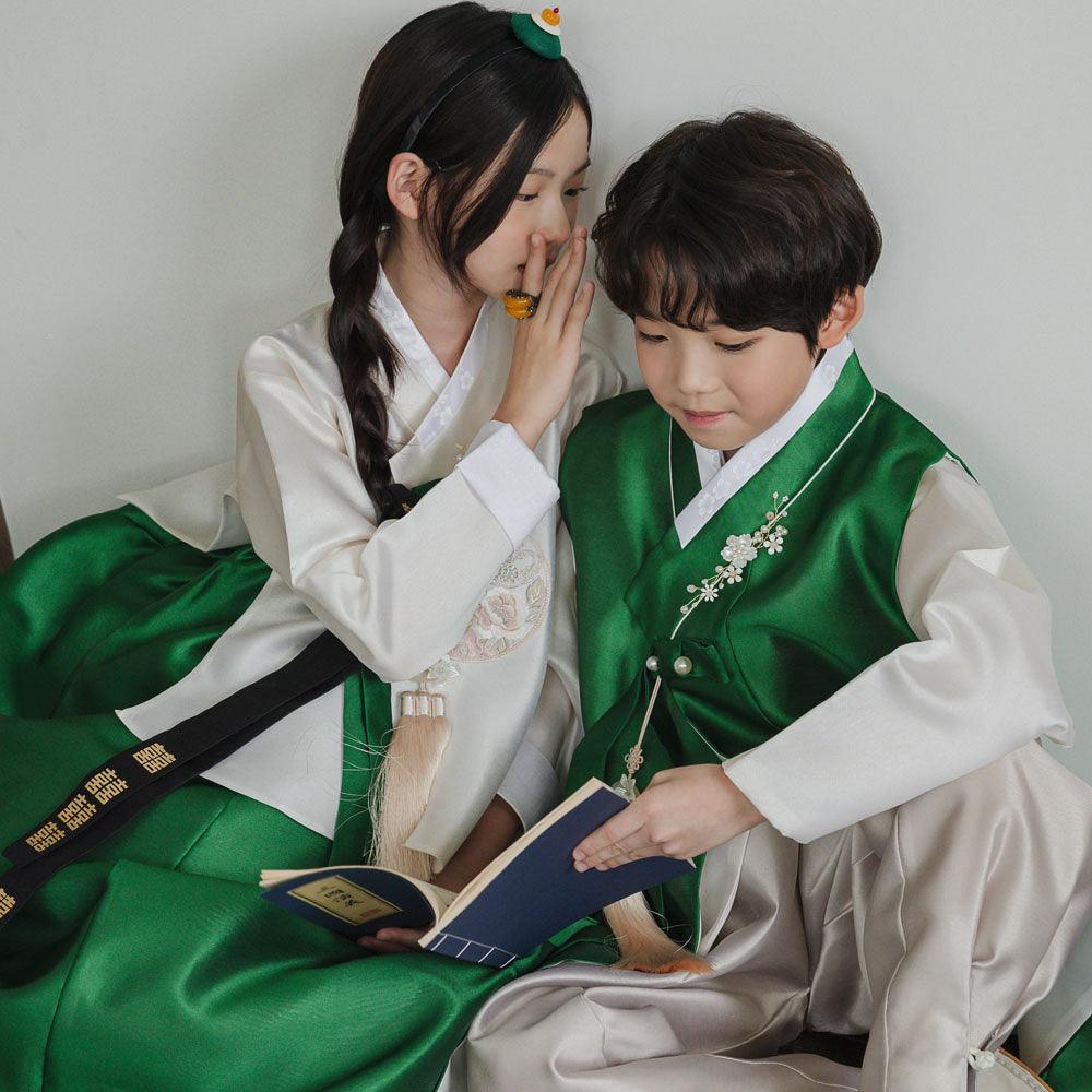 A child in a Native Korean Yoonwoo Green Boy Hanbok and a girl in a white Girl Hanbok reading a book.