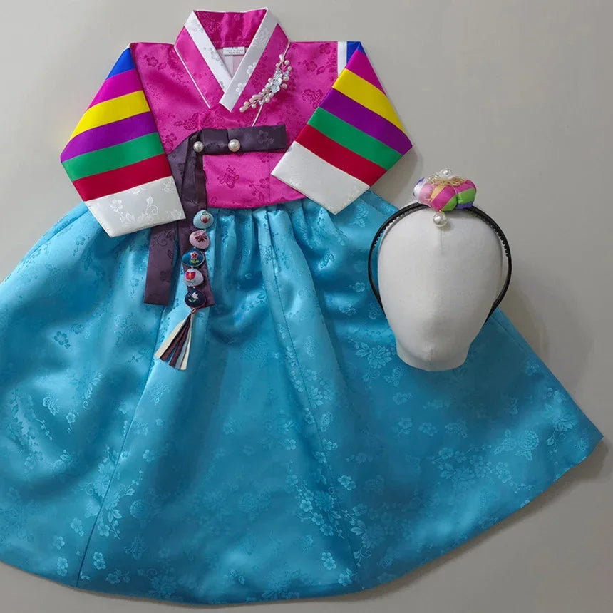Girl Hanbok featuring a pink Saekdong jeogori and a sky blue skirt with a matching headpiece.