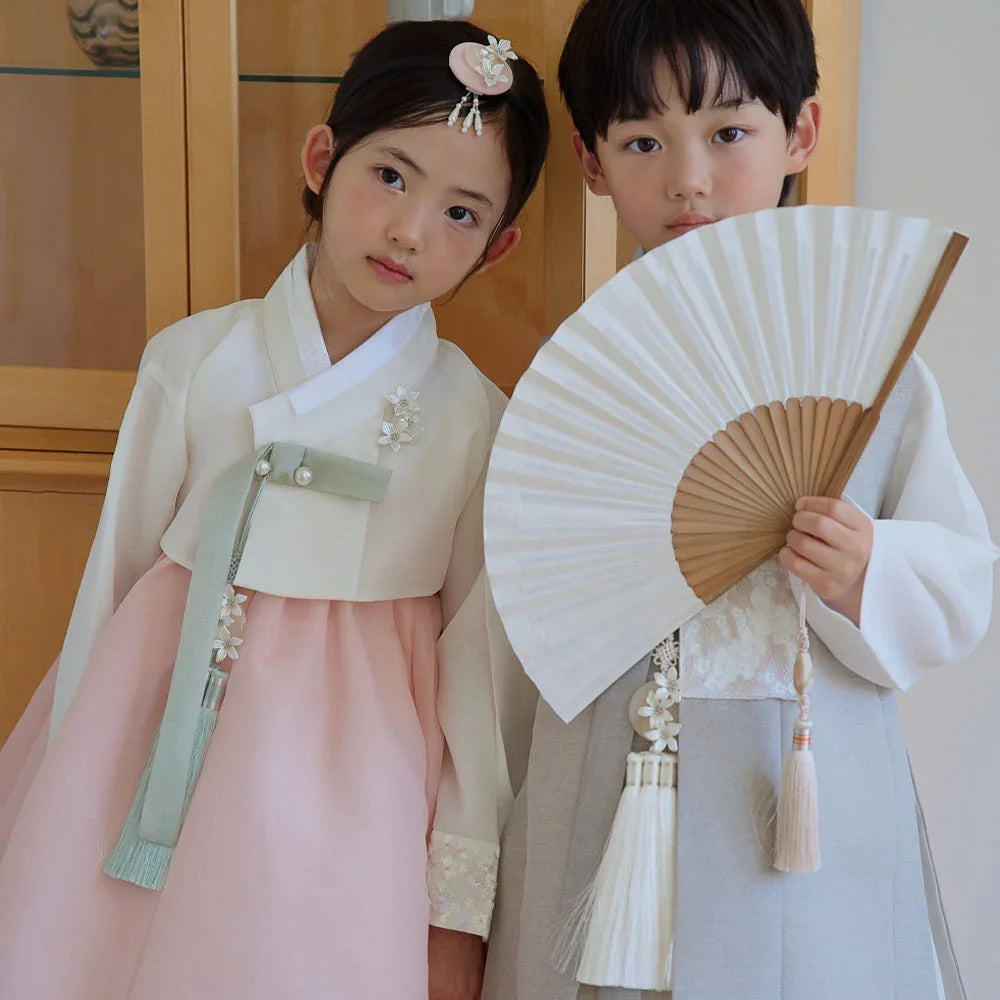 A young girl wearing a Yujin White Coral Girl Hanbok and a boy in a white and grey Boy Hanbok.