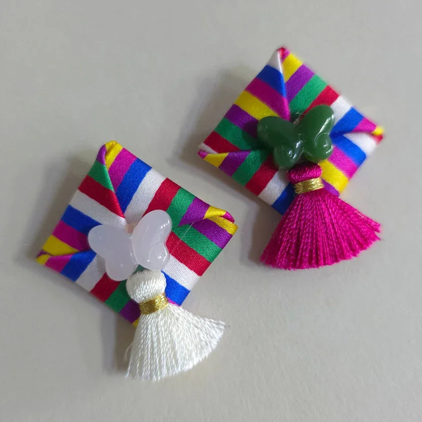 Two Native Korean Saekdong Ddakji brooches with colorful stripes, butterfly accents, and tassels.