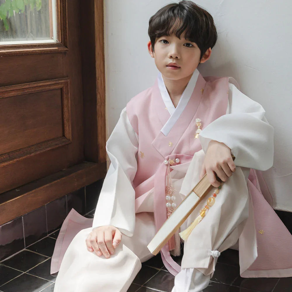 Young boy wearing a pink and white Native Korean boy hanbok holding a traditional fan.