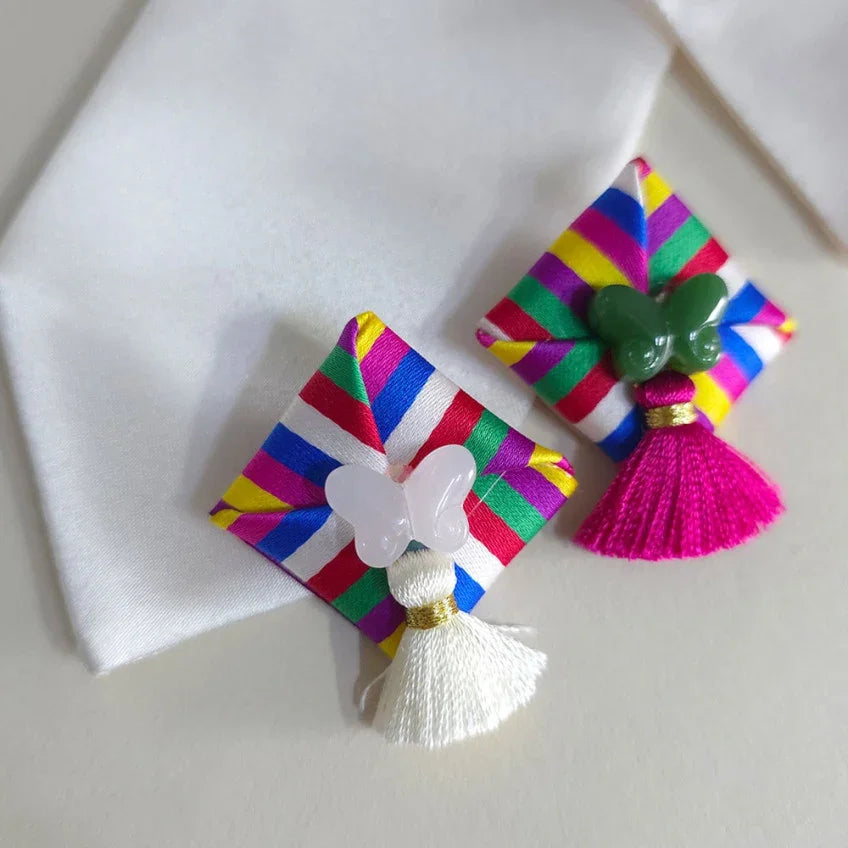Two Native Korean Saekdong Ddakji brooches with butterfly charms and tassels on white fabric.