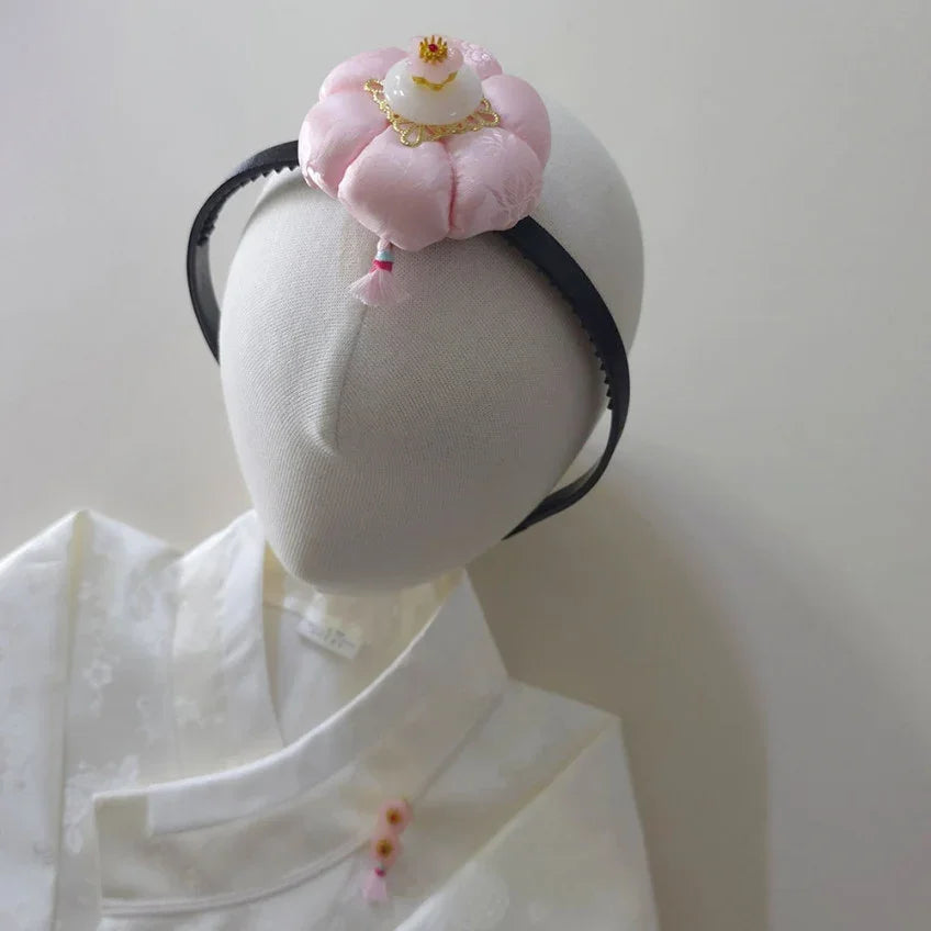 Native Korean pink Jokduri traditional headband on a white mannequin wearing a white hanbok.