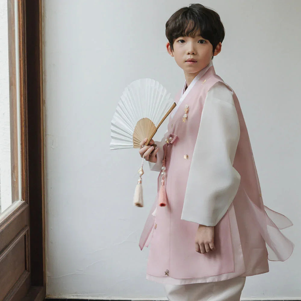 A young boy wearing a pink and white Native Korean Boy Hanbok holding a white folding fan.