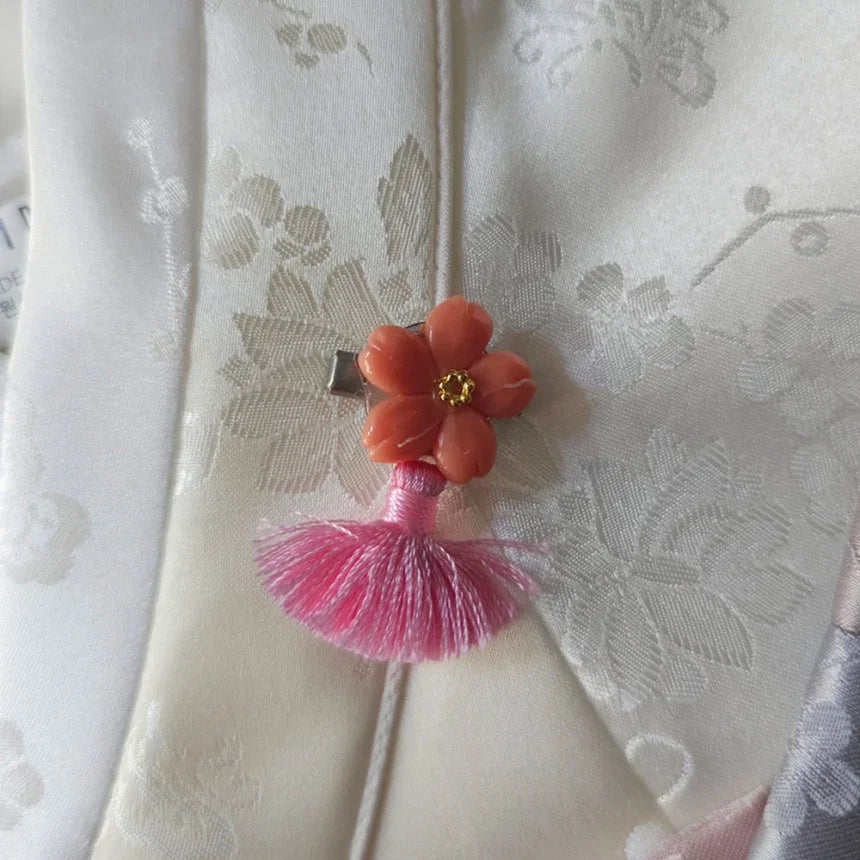 Close-up of a coral flower norigae accessory with a pink tassel on a white Native Korean hanbok.