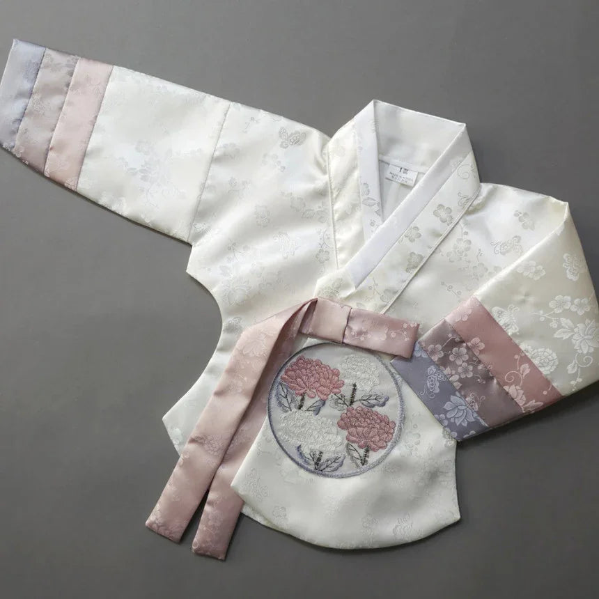 White silk Girl Hanbok jeogori with floral embroidery and pink ribbon ties.
