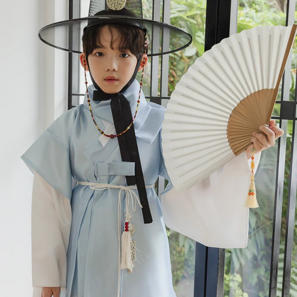 Boy wearing a light blue Native Korean Dopo Hanbok with a Gat and holding a white folding fan.