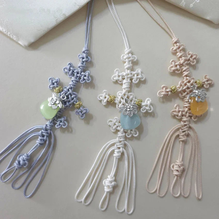 Three Native Korean charm knotted Norigae in purple, white, and beige with decorative gemstones.