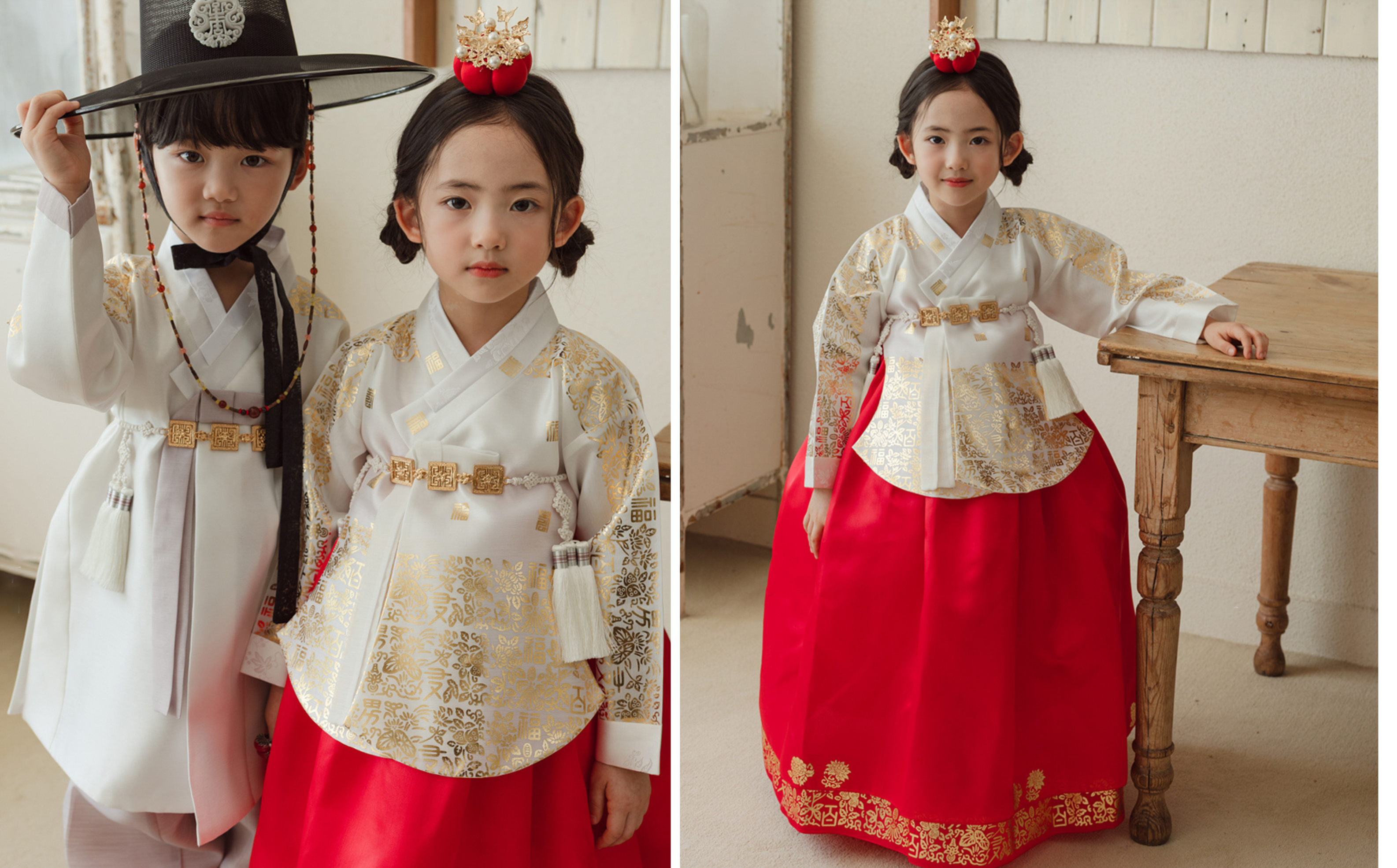 Two children in traditional Korean hanbok, one in white and gold and the other in red and gold, standing indoors.