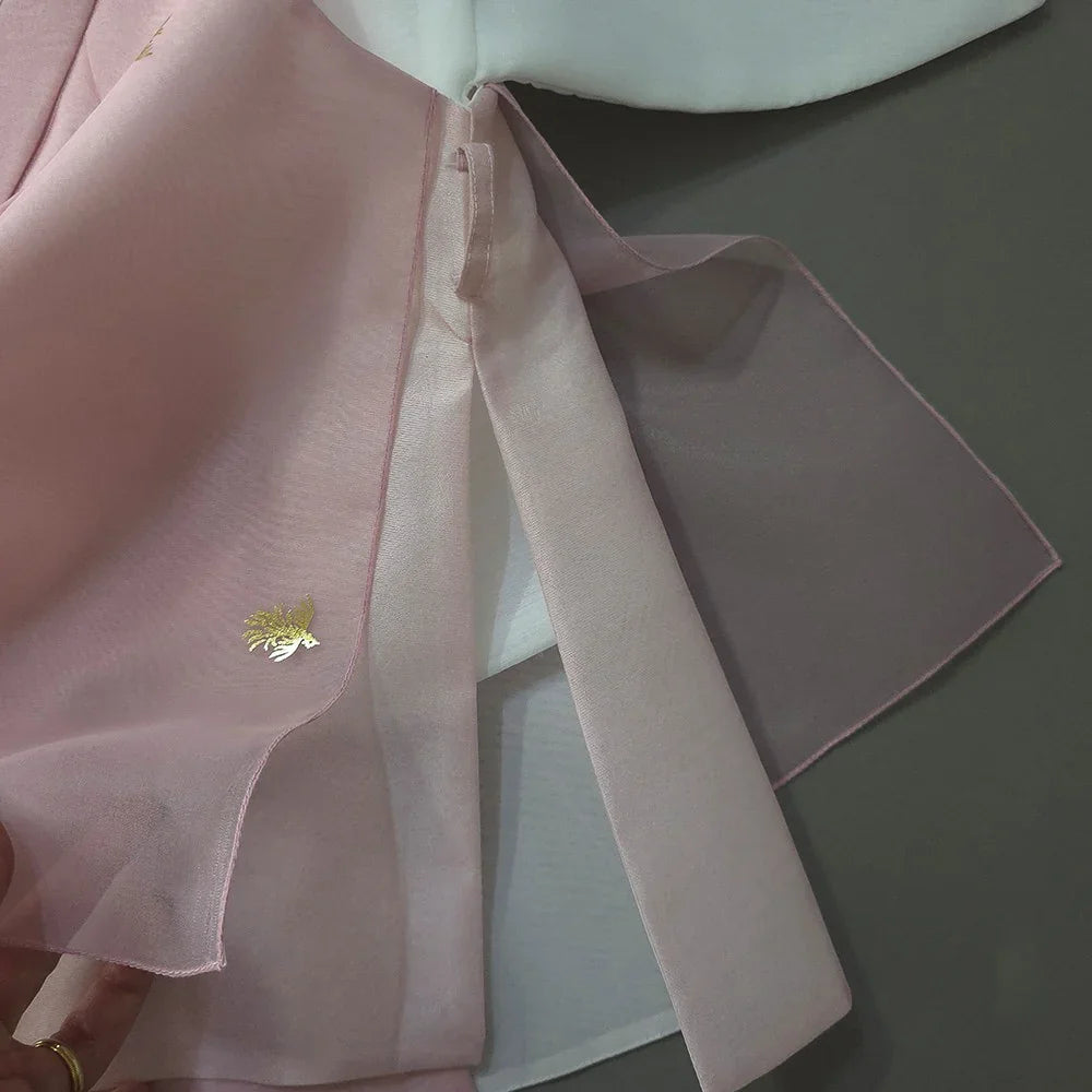 Close-up of the pink fabric and tie of a Heesung Boy Hanbok with gold embroidery.