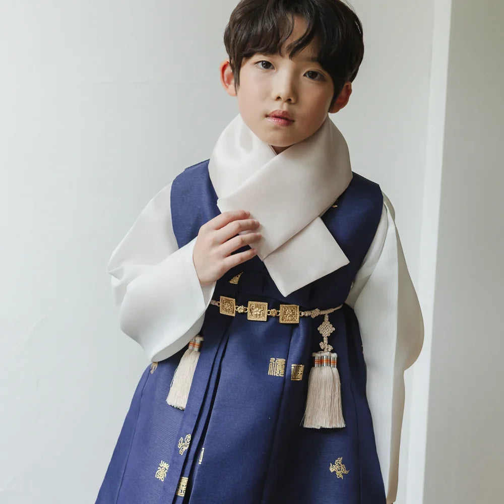 A young boy wearing a navy blue Native Korean boy hanbok with a white scarf and traditional Norigae.